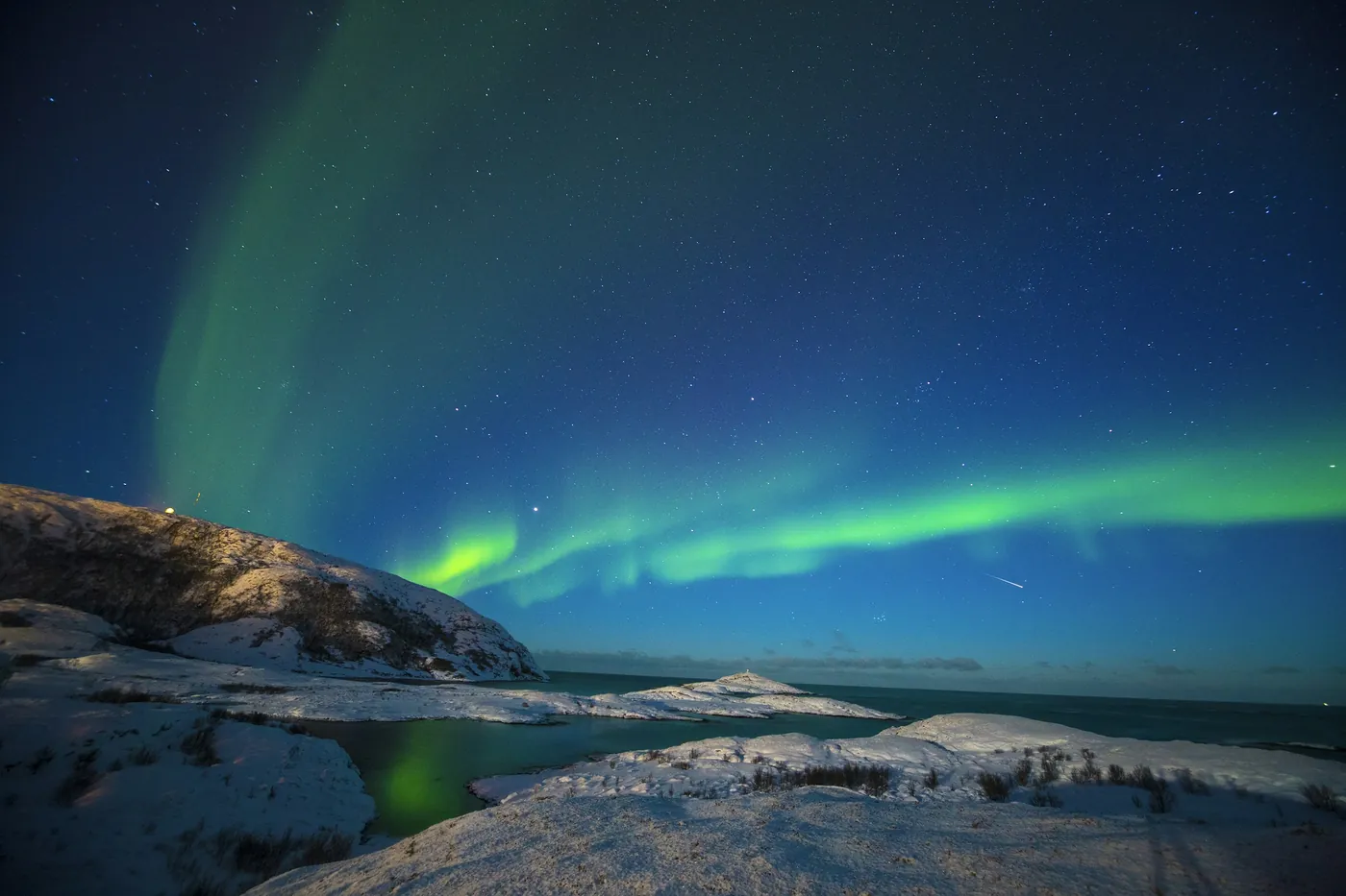 Green northern lights over a snowy coastline at night