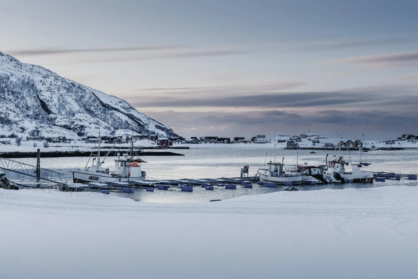 Snow-covered boats pulled up on the shore, mountains behind