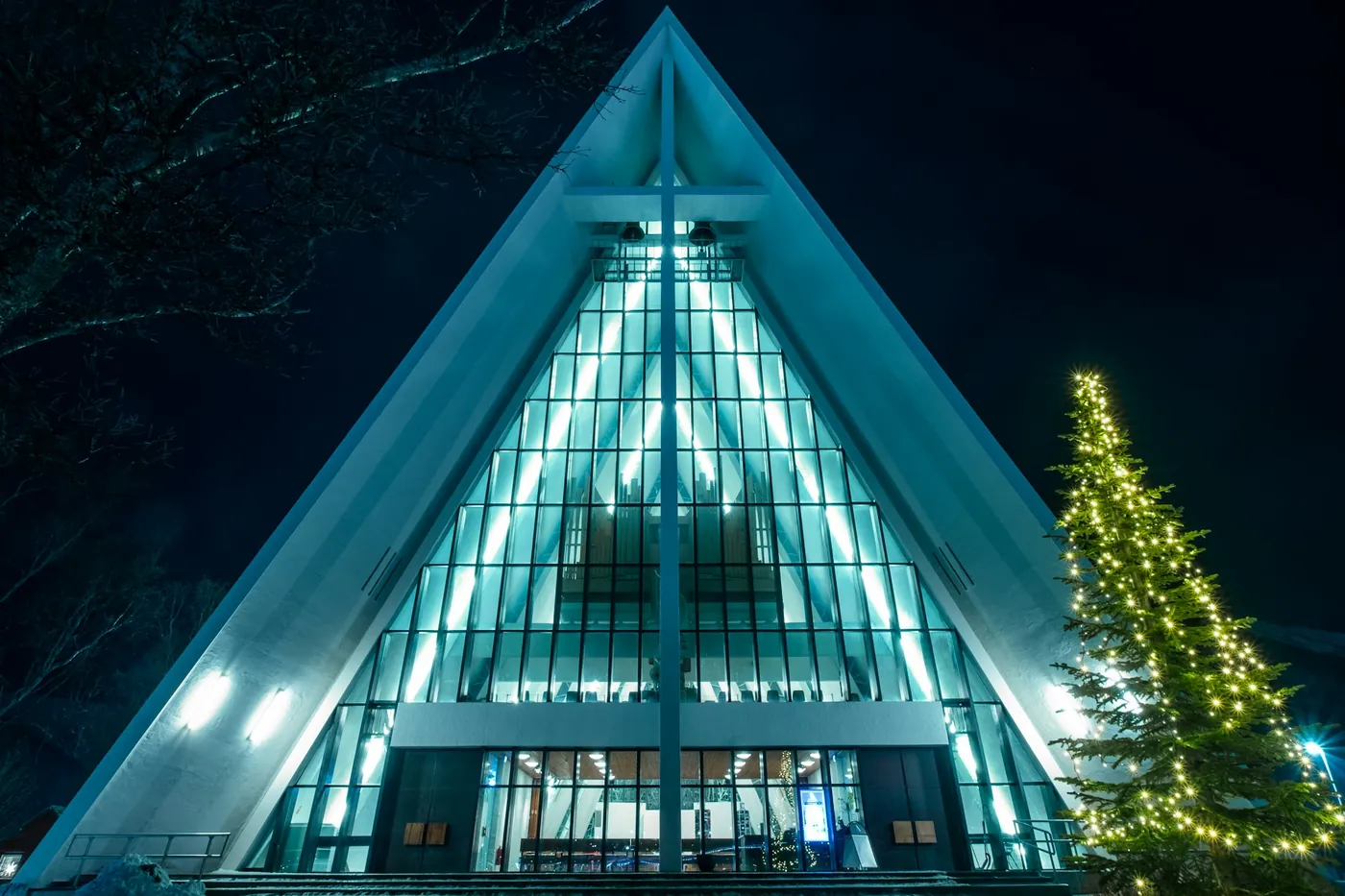 The Arctic Cathedral lit up at night with a Christmas tree in front