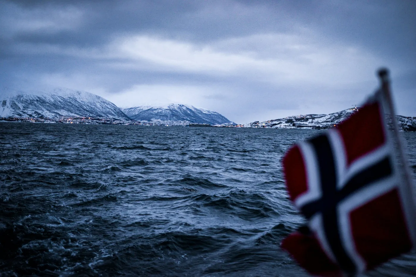 Mare mosso visto da una barca con la bandiera norvegese, montagne sullo sfondo