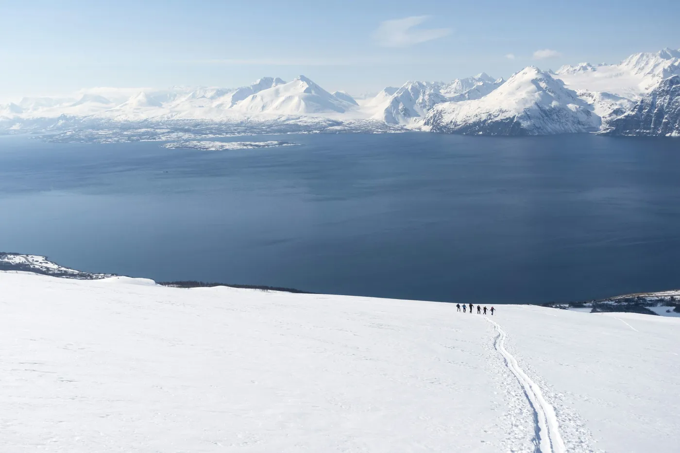 Ski tourers walking towards snow-covered mountains above the sea