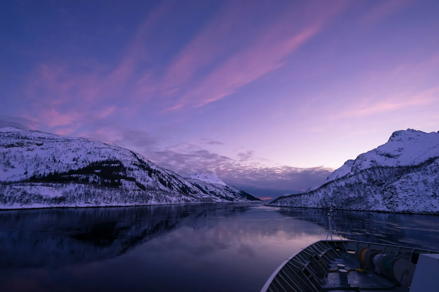 View from the deck of a ship across a fjord in purple twilight