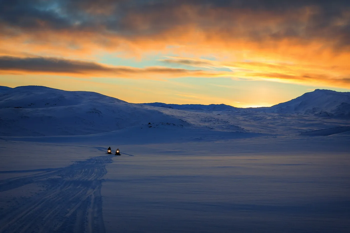 Two snowmobiles on a wide snowfield at sunset