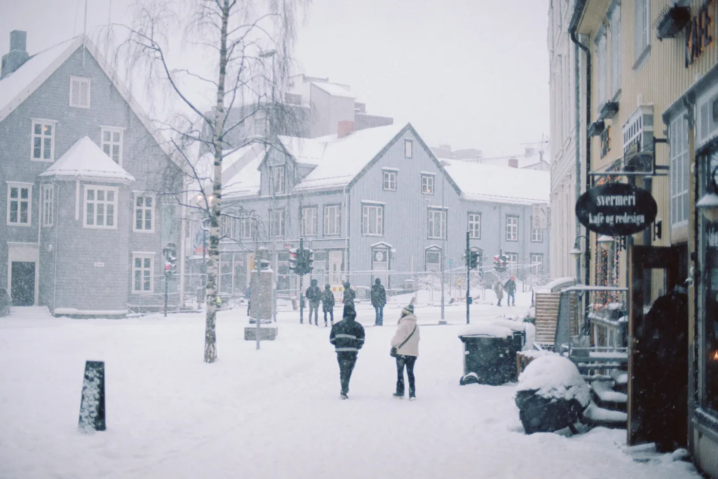 A snowy street lined with wooden houses in Tromsø, with people walking in falling snow